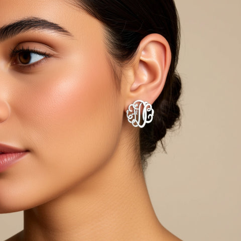 Close-up of a woman wearing silver monogram earrings against a beige background