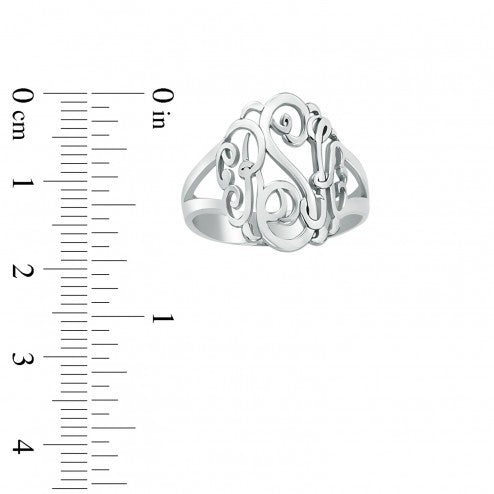 Silver ring with monogram design next to a ruler on a white background